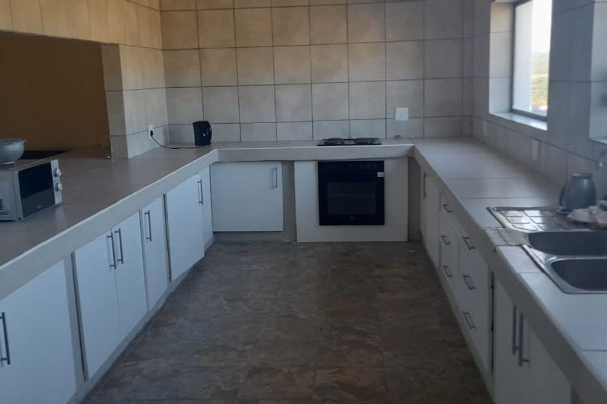 A functional kitchen featuring tiled countertops, built-in oven and hob, double basin sink, and ample white cabinetry with tiled splashbacks.