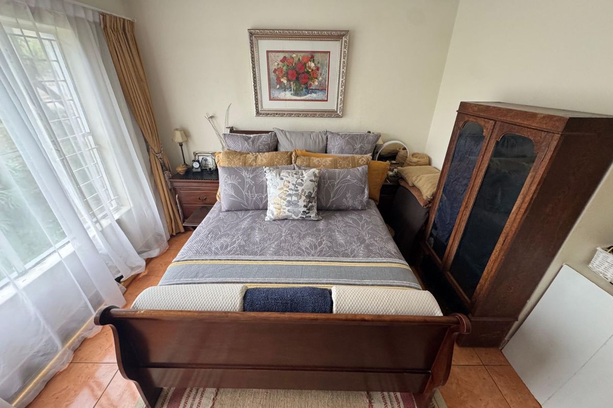 A bedroom featuring tiled flooring and a large window with curtains, providing natural light to the space.