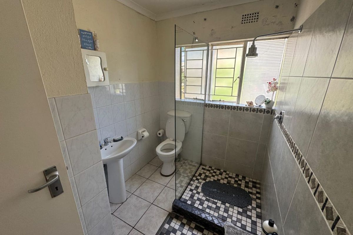 A functional bathroom featuring a pedestal basin, toilet, and a walk-in shower with a glass screen and tiled flooring.