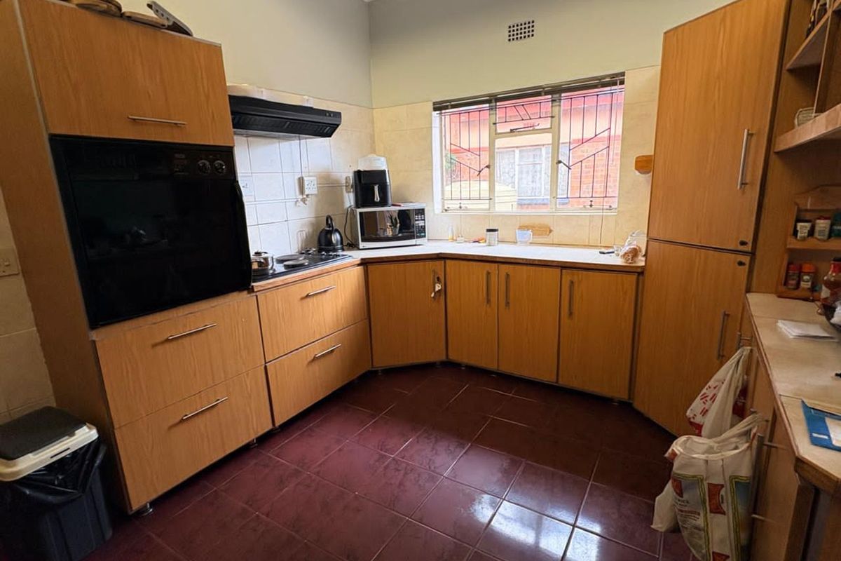 A functional kitchen featuring wood-look cabinetry, built-in oven, extractor fan, and tiled flooring with a window overlooking the exterior.