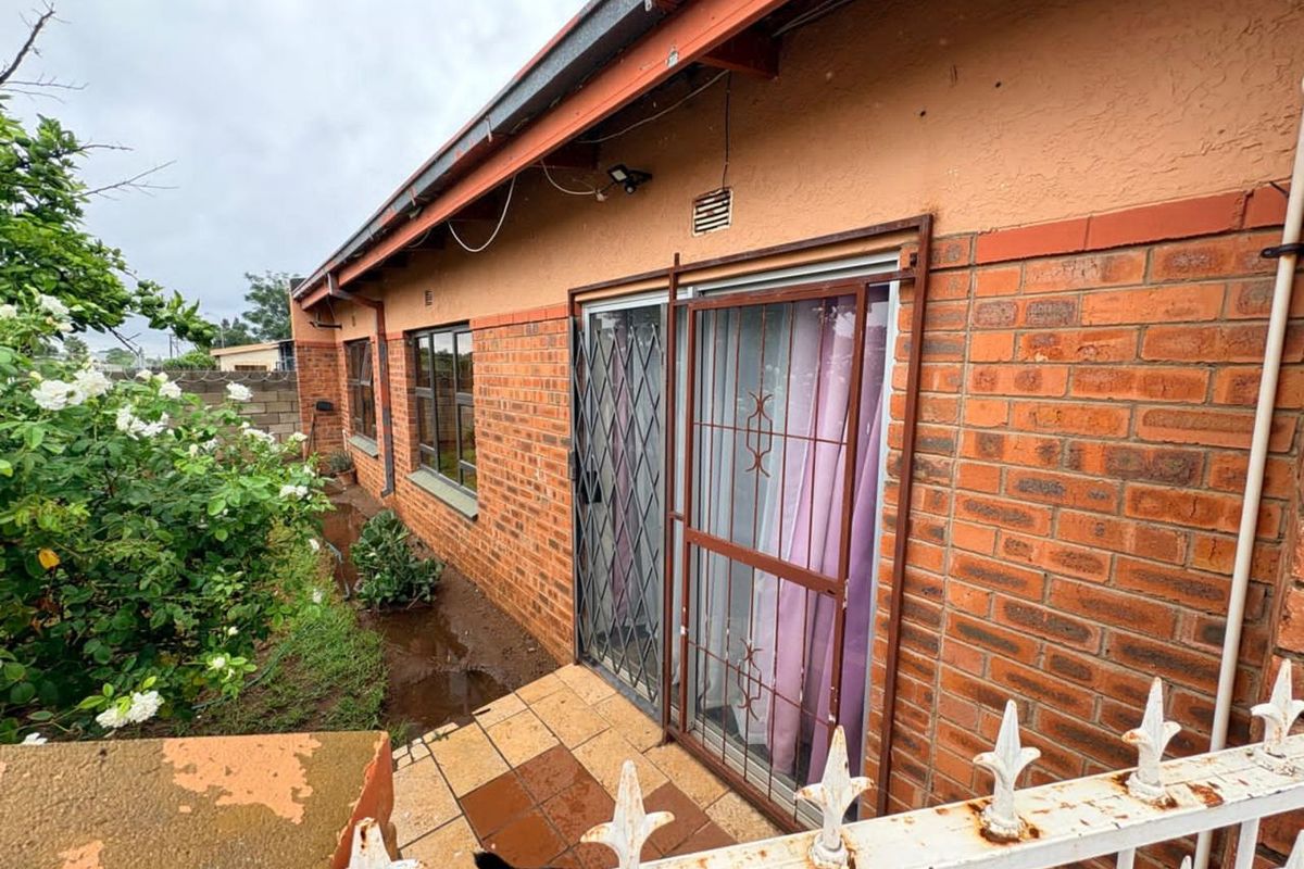 Rear exterior view of the house featuring face-brick walls, sliding glass doors with security gates, and a tiled patio area.