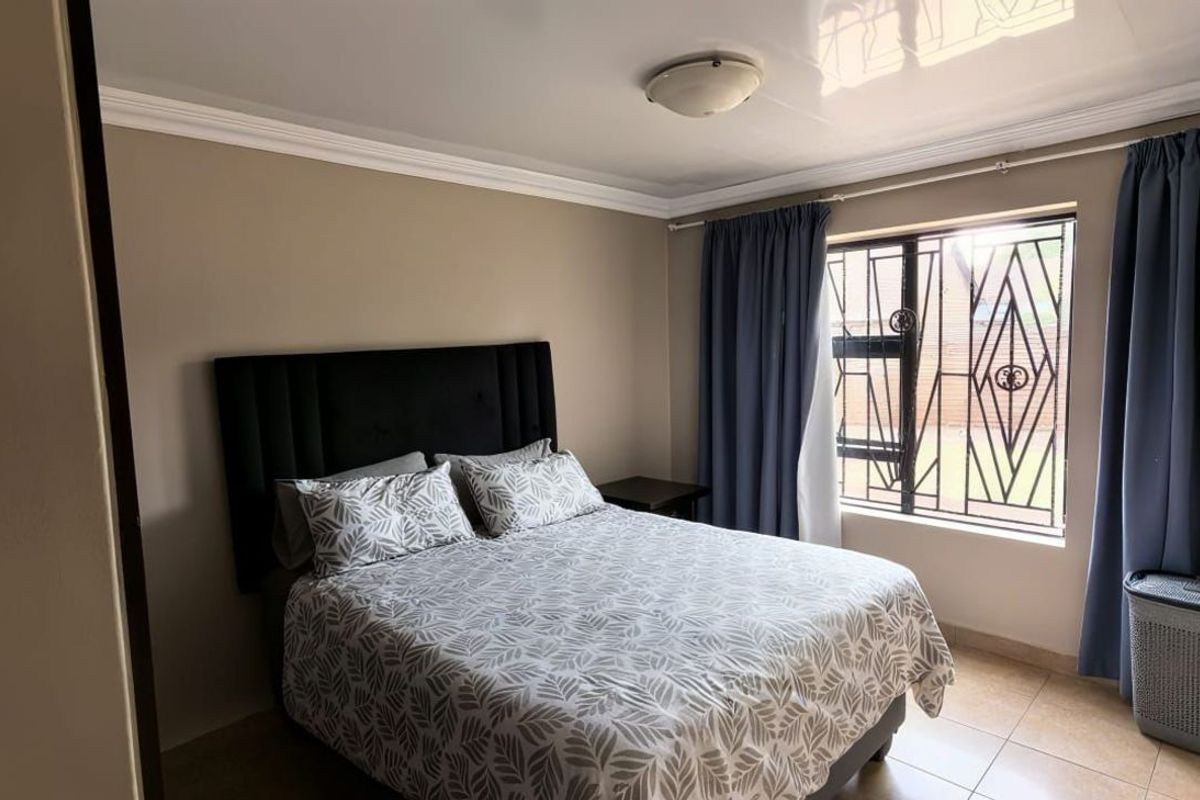A well-maintained bedroom featuring tiled flooring, crown molding, and a window fitted with security bars.