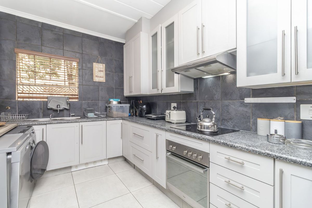 A functional kitchen featuring light grey cabinetry, granite countertops, a built-in oven with hob, extractor fan, and tiled splashbacks.