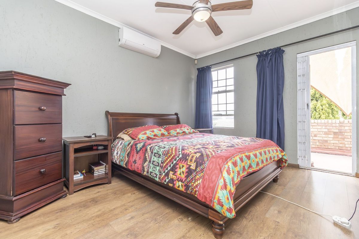 A bedroom featuring wood-look flooring, a ceiling fan, wall-mounted air conditioning unit, and direct access to an outdoor patio area.