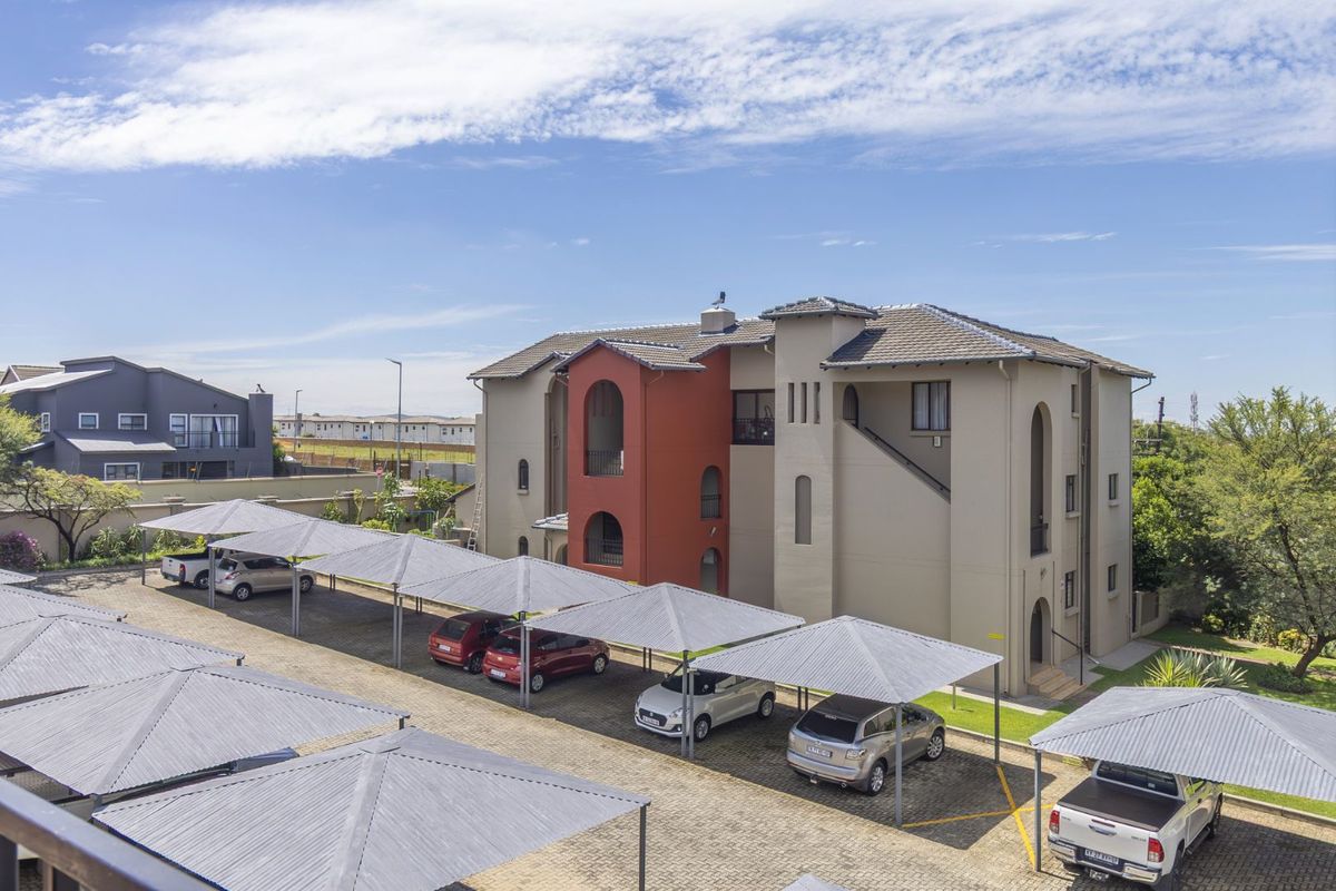 An elevated view of a multi-story residential building featuring a paved parking area with multiple covered carports.