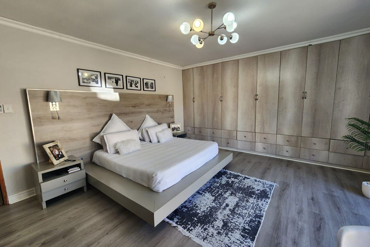 Spacious bedroom featuring extensive built-in cabinetry, modern wood-look flooring, and a contemporary light fixture.