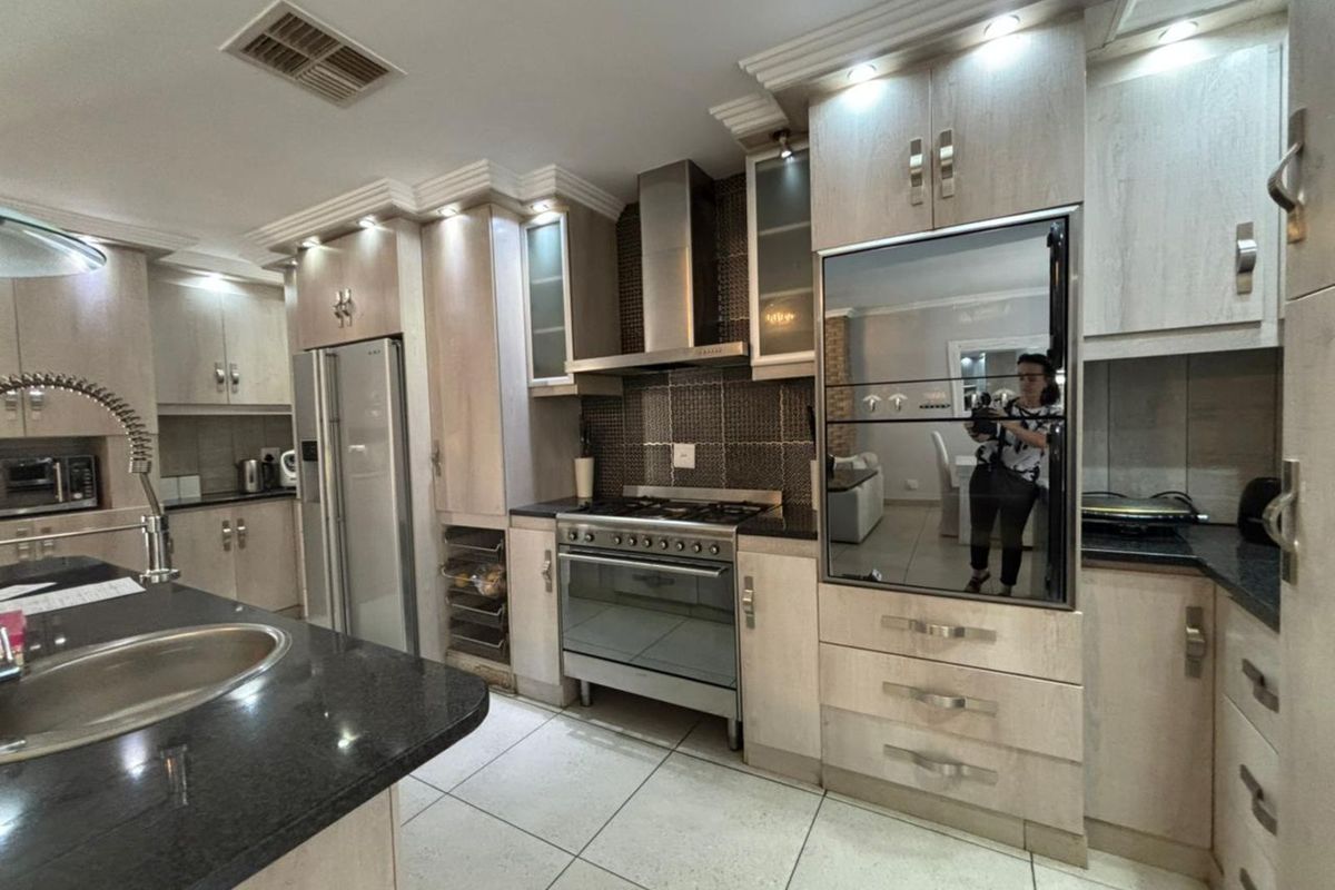 Modern kitchen featuring light wood cabinetry, granite countertops, a central island with a prep sink, and a stainless steel gas stove with extractor fan.
