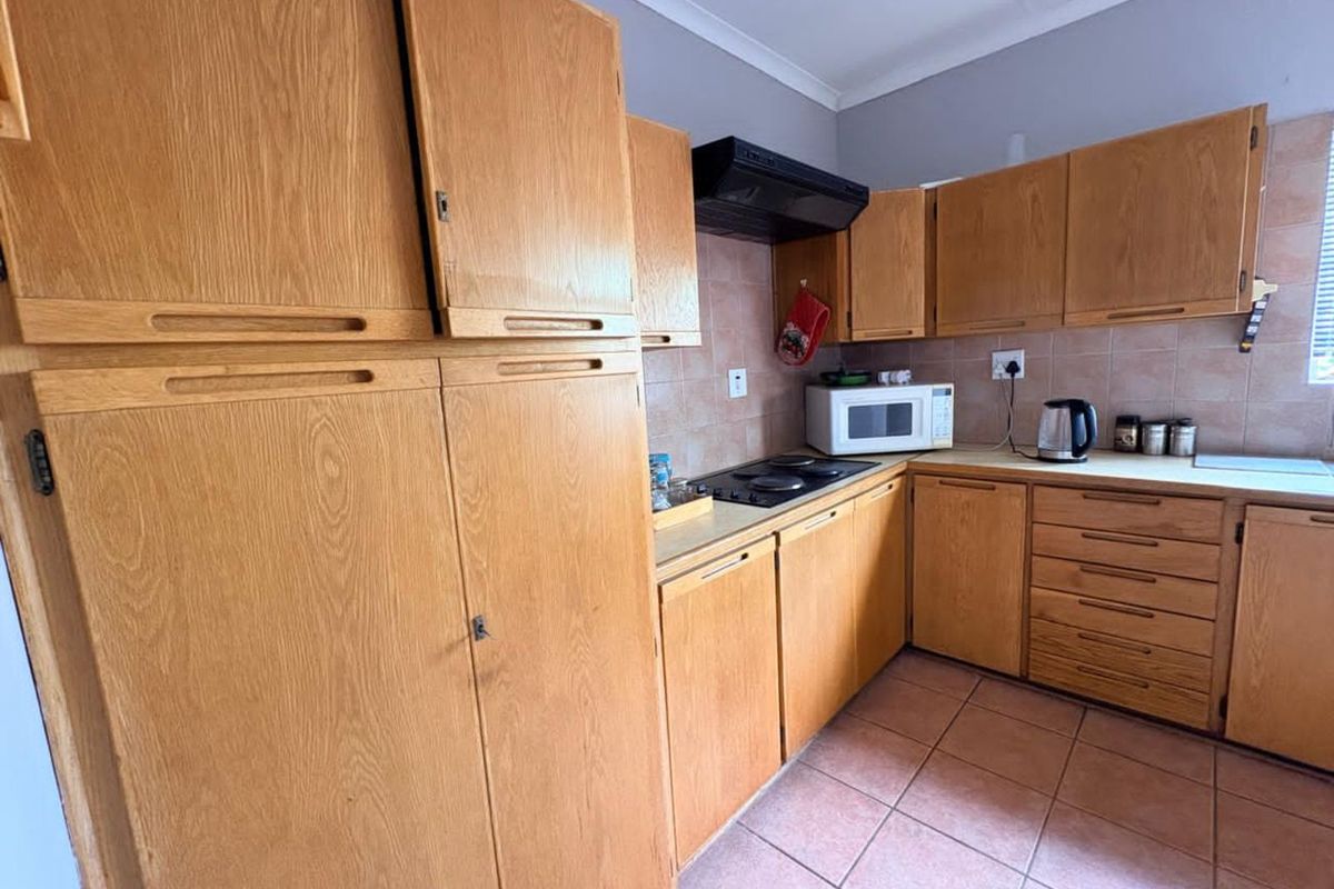 A functional kitchen featuring traditional wood-finish cabinetry, tiled splashbacks, a built-in hob, and an extractor fan, offering a classic layout with ample storage space.