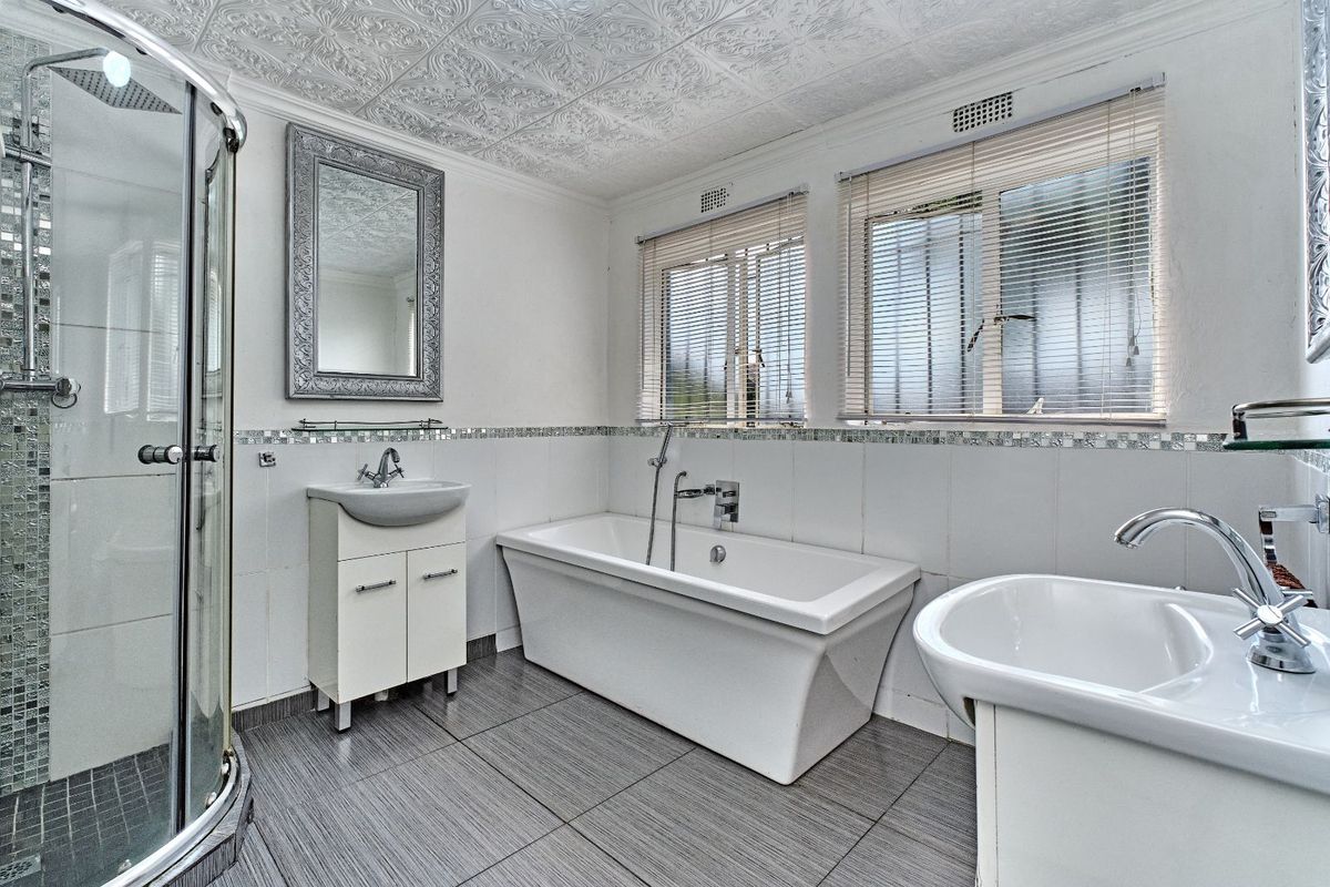A well-maintained bathroom featuring a glass-enclosed shower, a modern freestanding bathtub, a vanity basin, and tiled flooring with decorative wall accents.