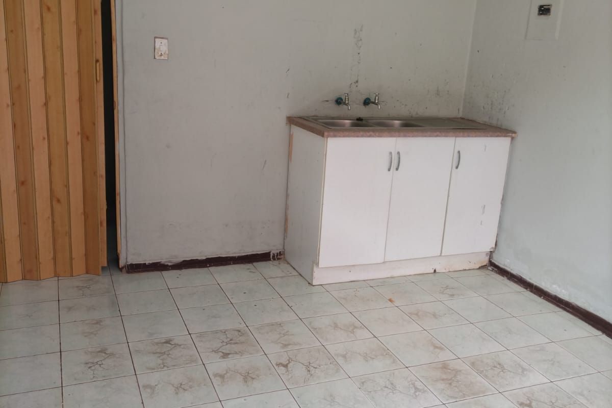 A basic kitchen area featuring a small sink unit, tiled flooring, and a folding wooden door, requiring significant renovation and cosmetic updates.
