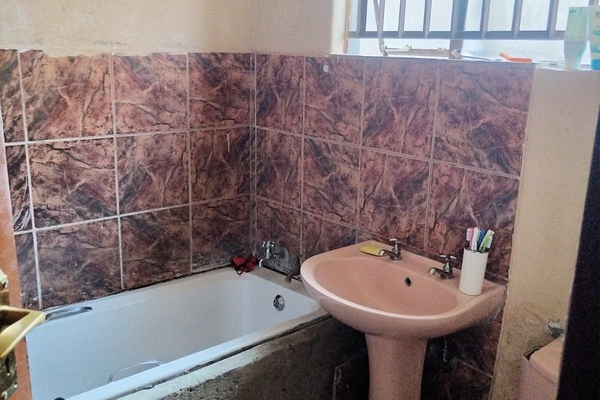 A dated bathroom featuring a pedestal sink, toilet, and bathtub with unfinished masonry surround and tiled walls.