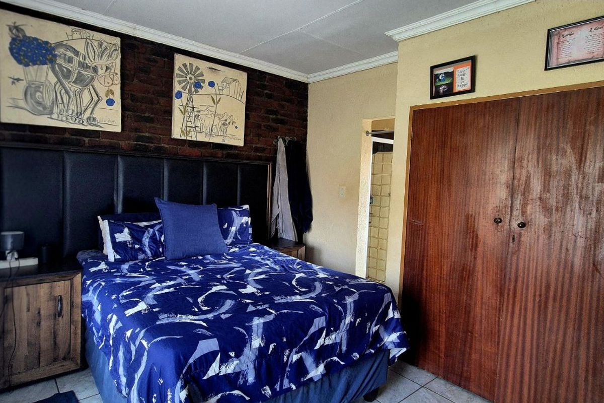 A bedroom featuring a dark brick accent wall, built-in wooden cupboards, and tiled flooring.