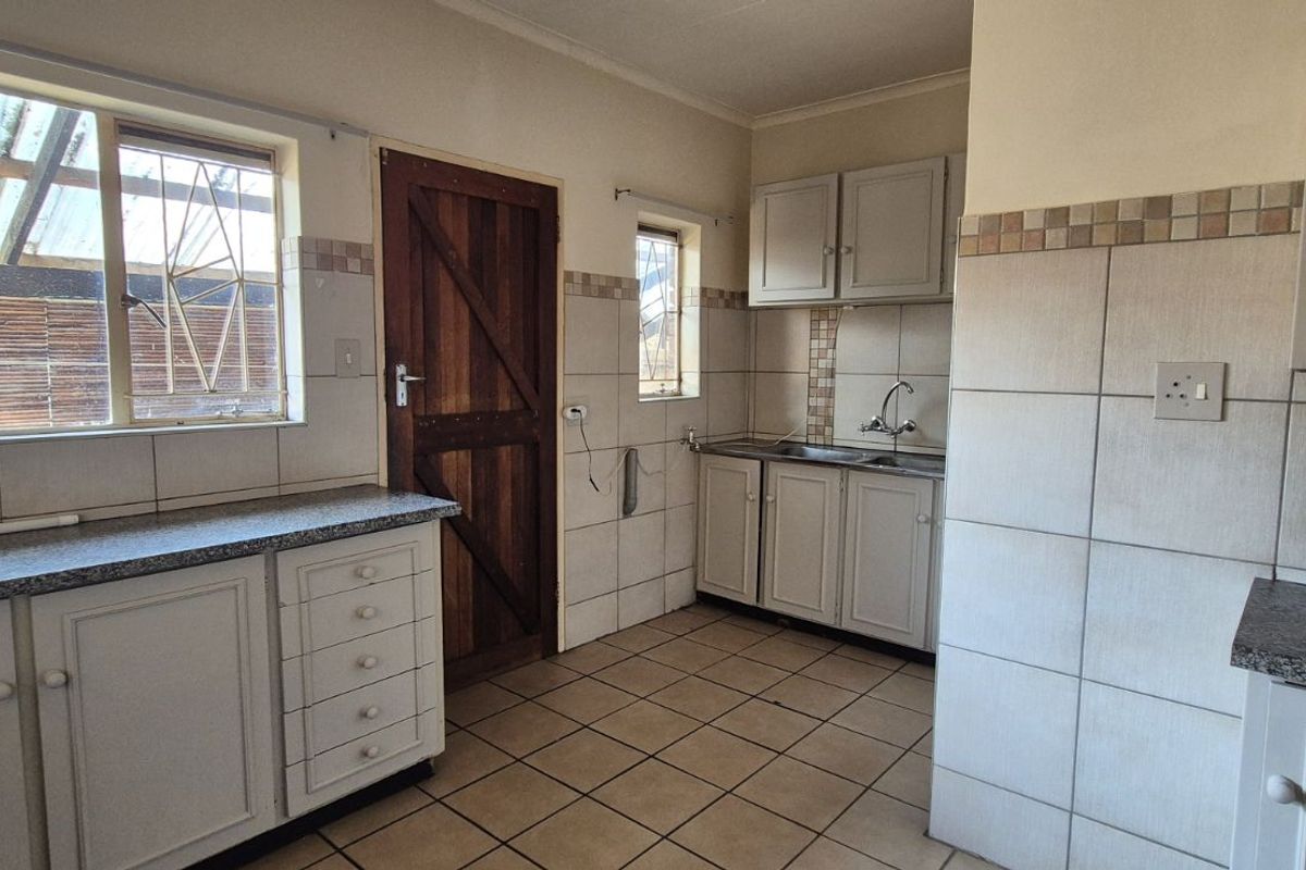 A functional kitchen featuring tiled flooring, neutral cabinetry, granite-look countertops, and a wooden exterior door leading to the rear of the property.
