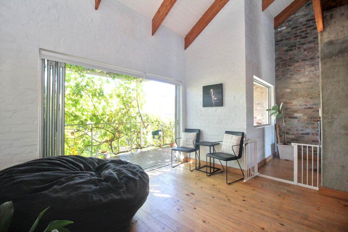 Bright living area featuring vaulted ceilings with exposed timber beams, rustic brick feature wall, timber flooring, and large sliding doors opening to a balcony.