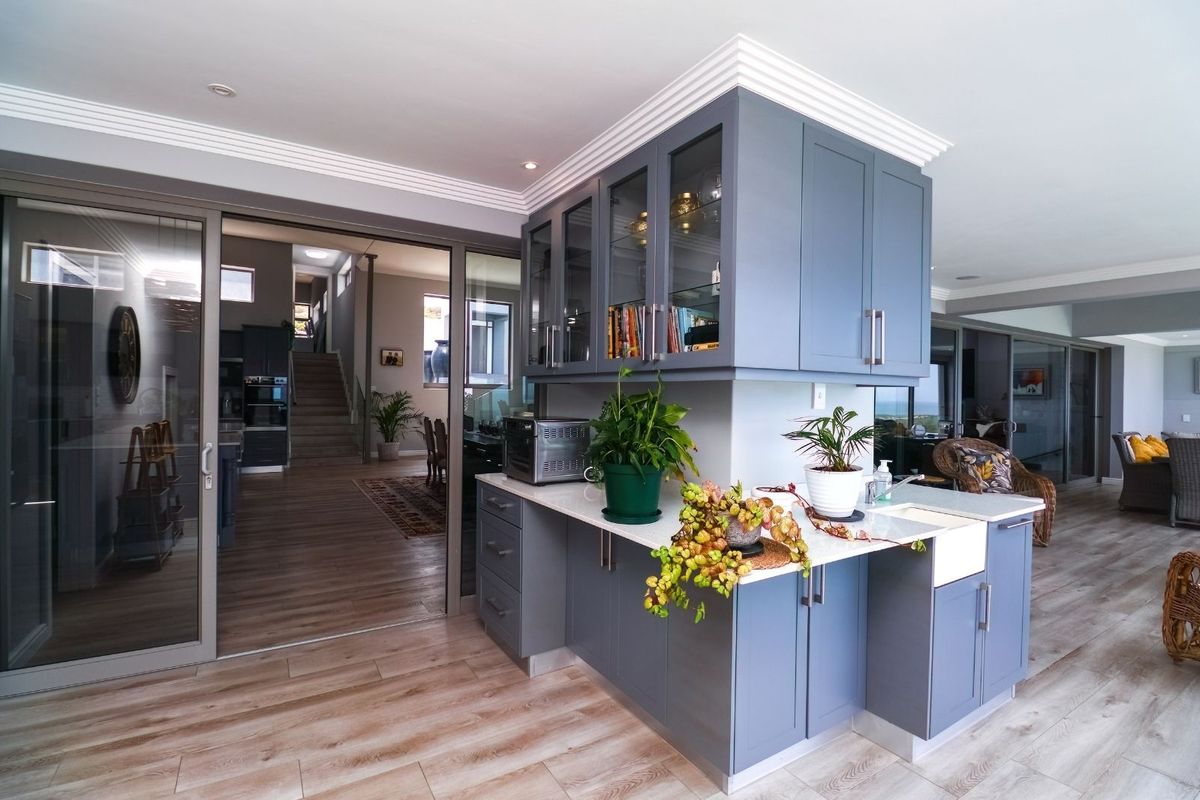 A modern kitchen area featuring custom blue cabinetry, stone countertops, and a farmhouse-style sink, seamlessly integrated into an open-plan living space.