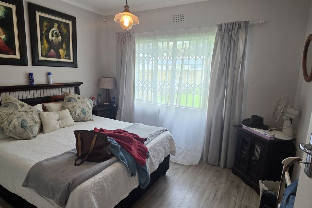 A well-maintained bedroom featuring light wood-look flooring, a window with security gate, and a central pendant light fixture.