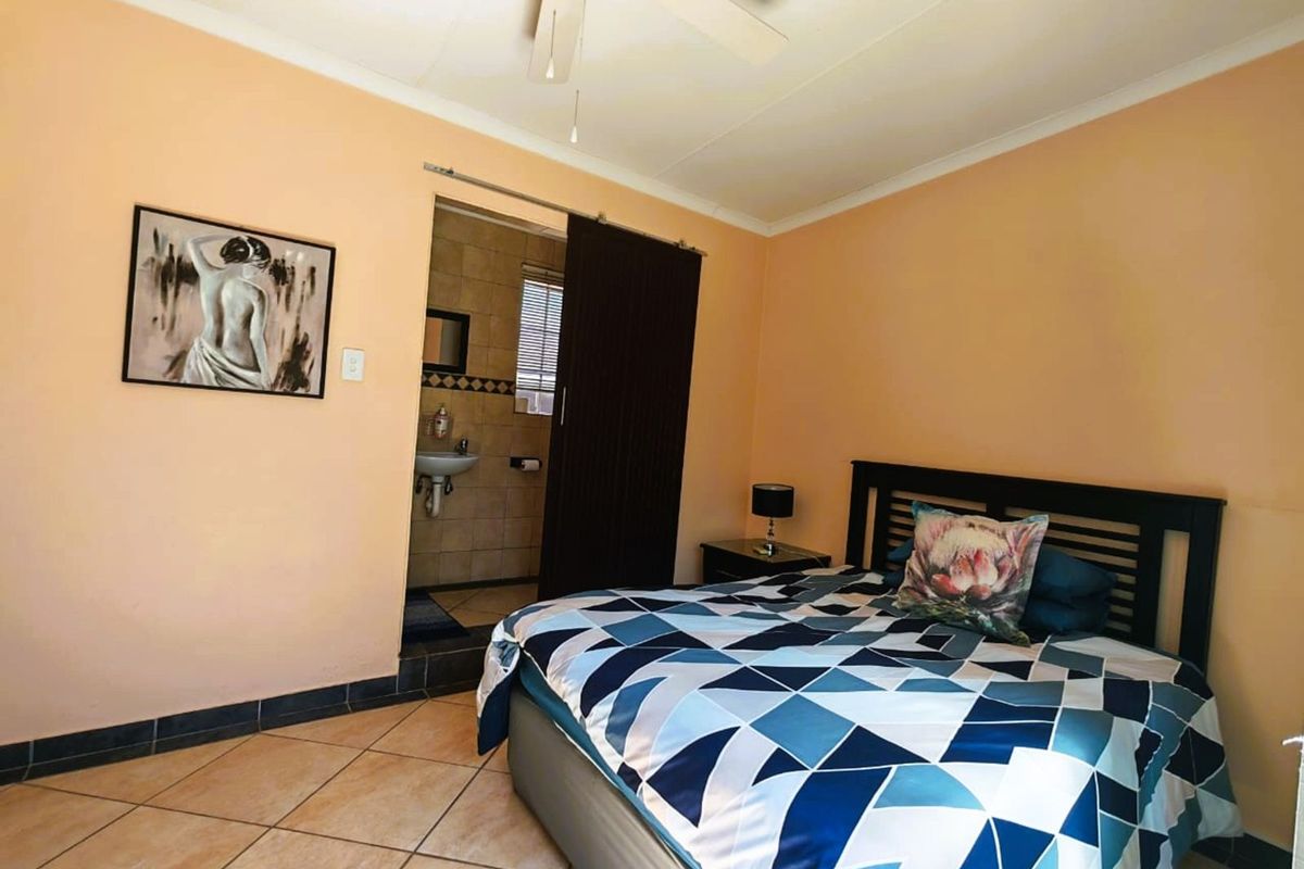 A bedroom featuring tiled flooring, a ceiling fan, and an en-suite bathroom accessed via a sliding door.