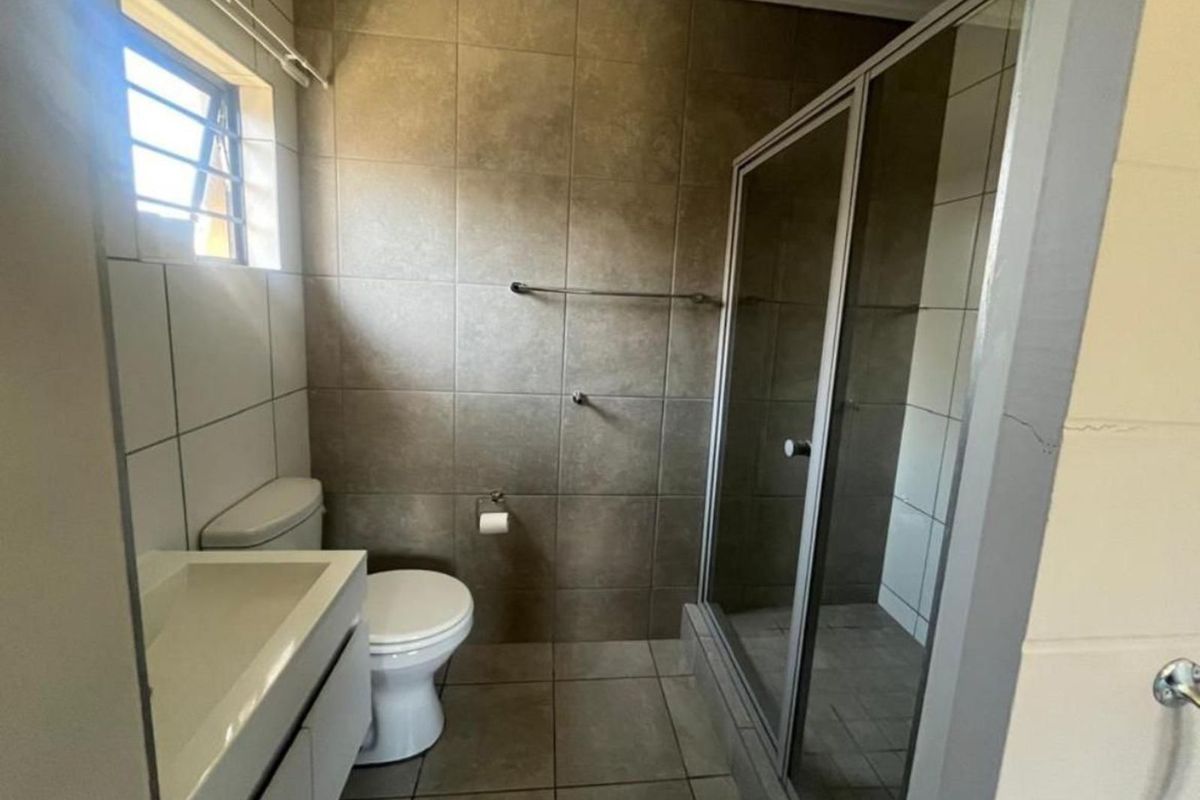A functional bathroom featuring a glass-enclosed shower, a modern vanity basin, and a toilet, finished with neutral wall and floor tiling.
