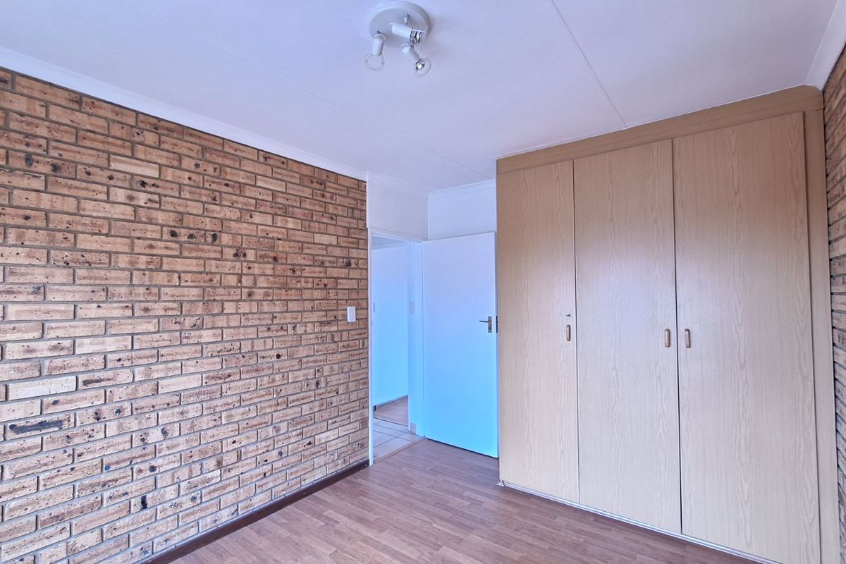 A bedroom featuring a distinctive exposed brick feature wall, built-in wooden cabinetry, and laminate flooring, offering a functional and neutral living space.