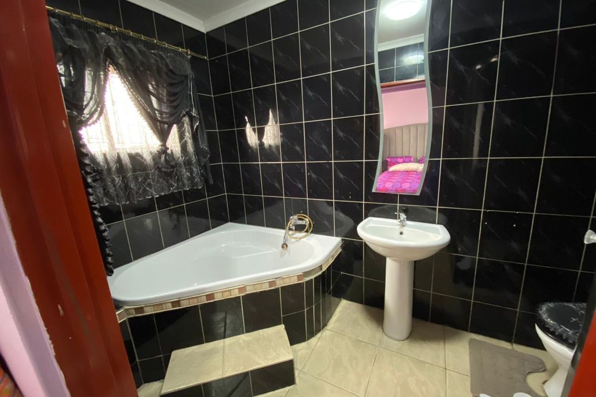 Bathroom featuring black wall tiling, a corner bathtub with a tiled step, and a white pedestal basin.