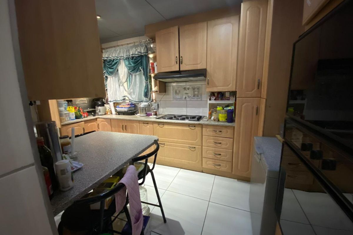 A functional kitchen featuring light wood cabinetry, a built-in hob with extractor fan, and a breakfast bar with tiled flooring.