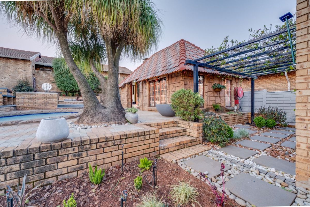 A well-maintained rear garden area featuring a paved patio, brick retaining walls, a pergola, and a swimming pool with established landscaping.