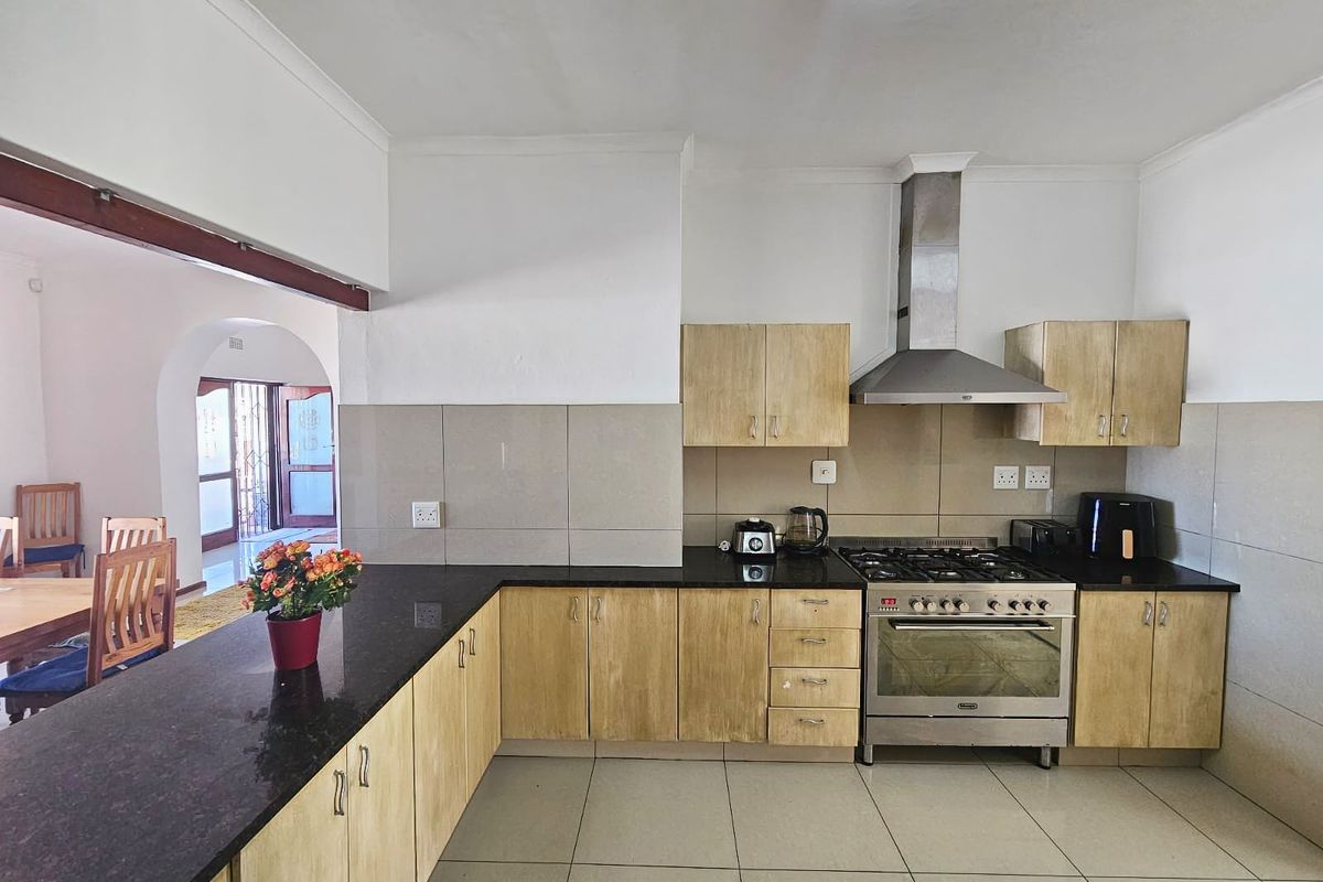 A functional kitchen featuring light wood cabinetry, dark granite countertops, a stainless steel gas stove with extractor fan, and neutral floor tiling.