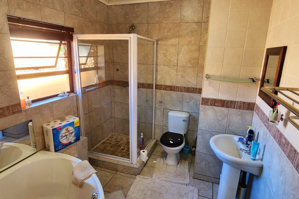 A functional bathroom featuring a corner bathtub, separate glass-enclosed shower, pedestal basin, and tiled walls with decorative border accents.