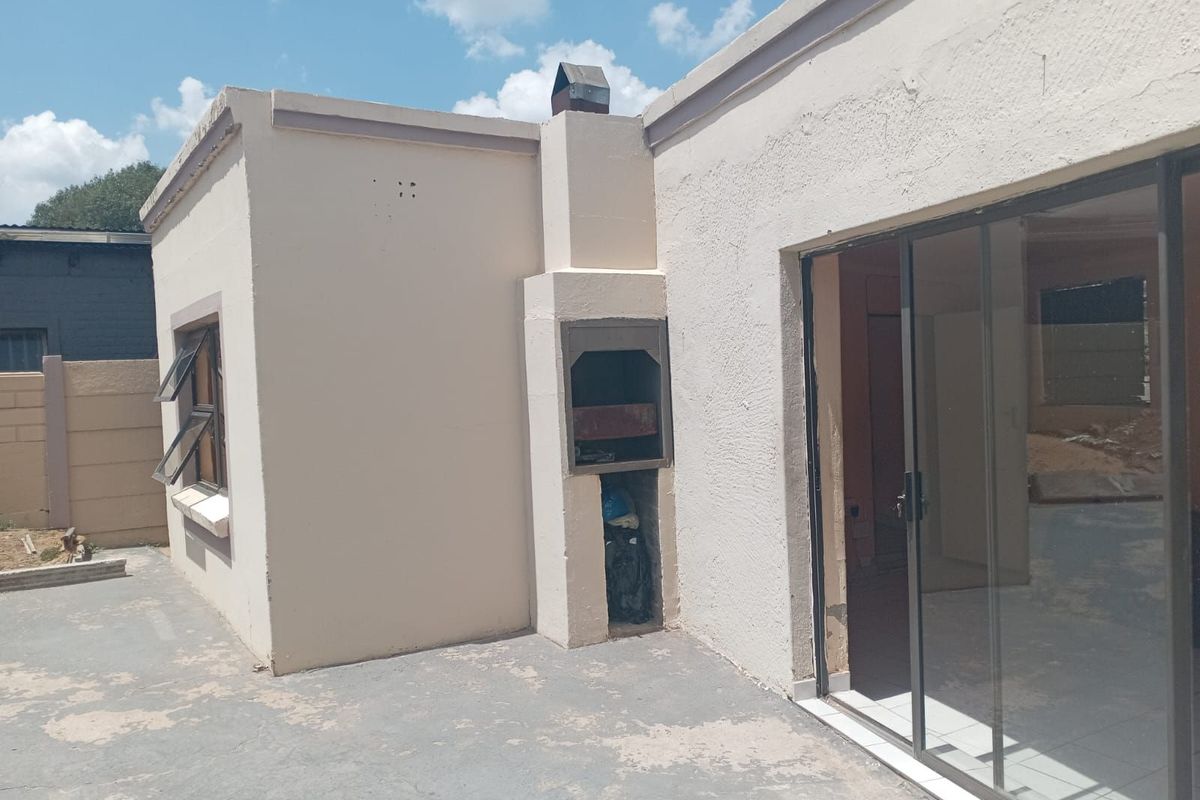 Exterior view of the rear patio featuring a built-in braai fireplace and sliding glass doors leading into the home.