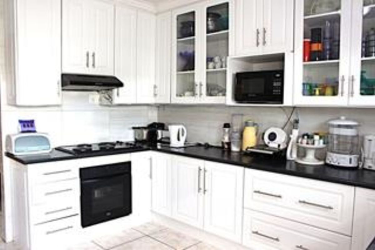 A functional kitchen featuring white cabinetry, dark countertops, a built-in oven, gas hob, and an integrated extractor fan.