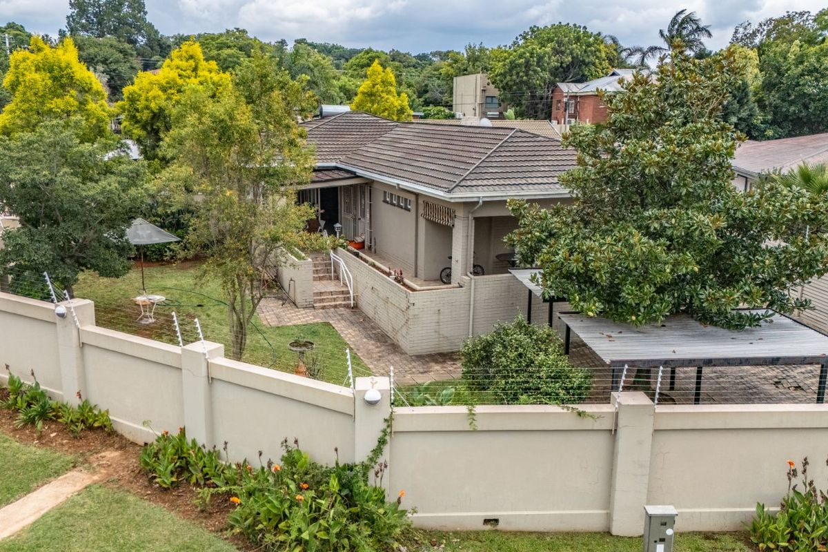 Aerial view of a residential property featuring a tiled roof, perimeter wall with electric fencing, paved patio area, and established garden.