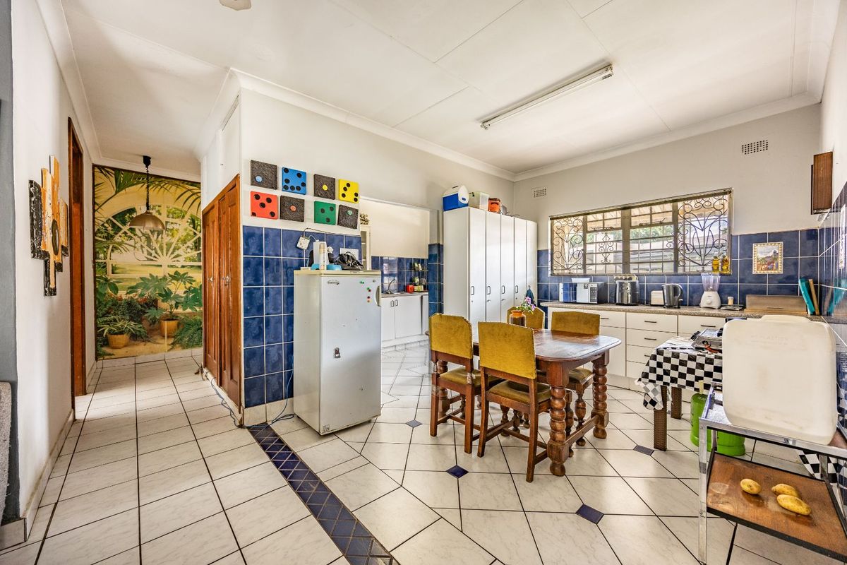 A functional kitchen and dining area featuring tiled flooring, blue wall tiles, built-in cabinetry, and security bars on the windows.