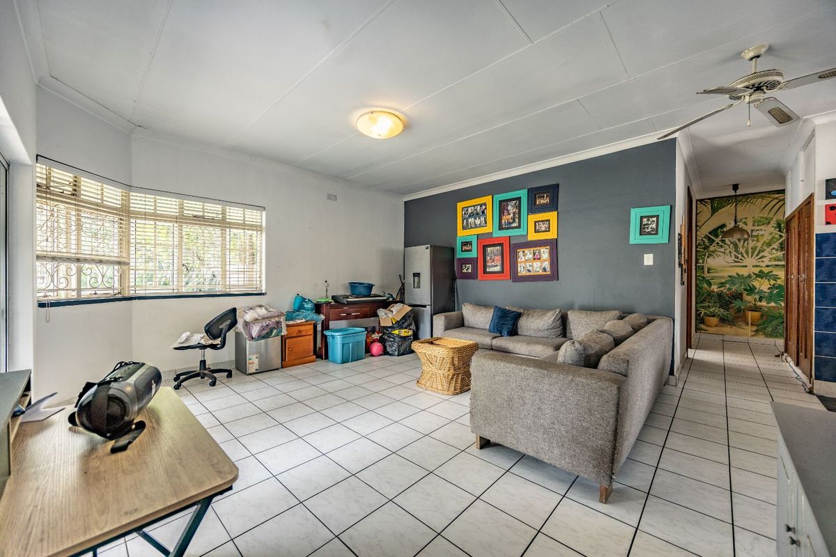 Spacious living area featuring tiled flooring, a ceiling fan, and a large window with security bars, offering a functional layout for family living.