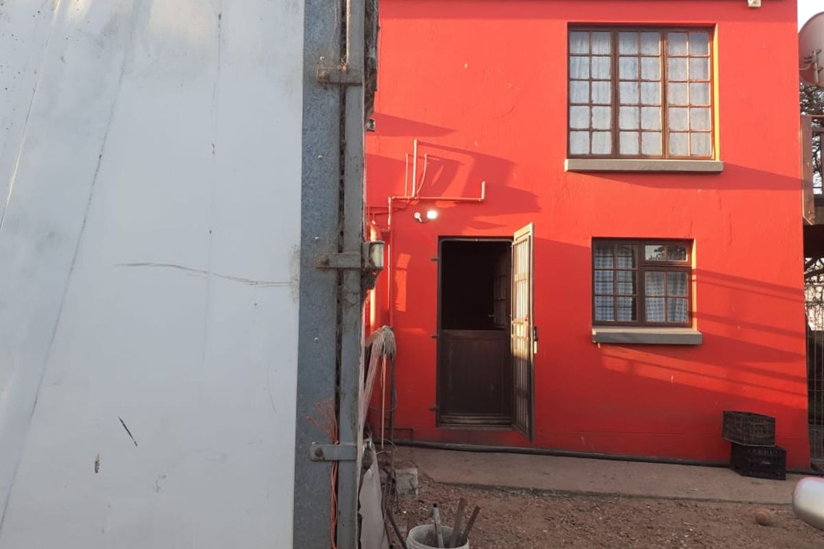 Rear exterior view of a retail property featuring a bright red facade, multi-pane windows, and a secure entrance door.