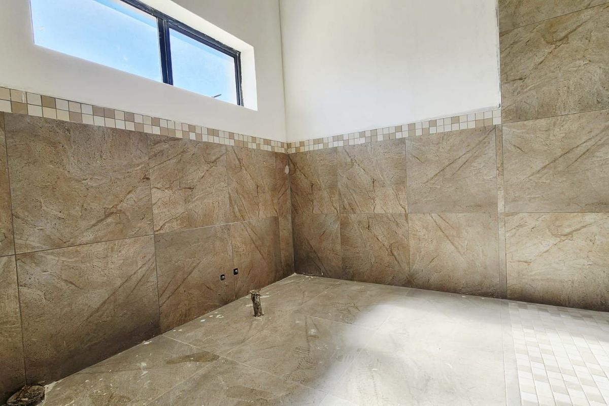 An unfinished bathroom space featuring large-format brown wall tiles, mosaic accent borders, and floor tiling, awaiting final fixture installation.