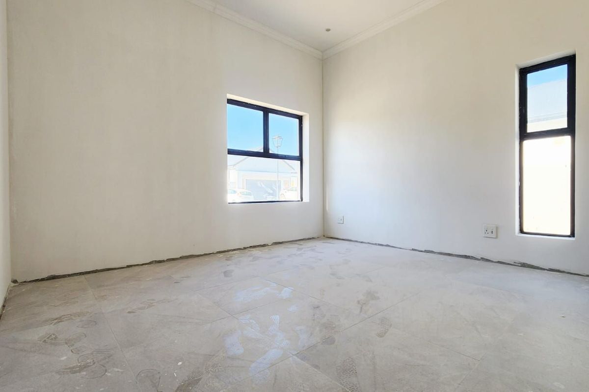 An empty, unfinished bedroom featuring tiled flooring, white walls, and modern black-framed windows, awaiting final touches and skirting installation.