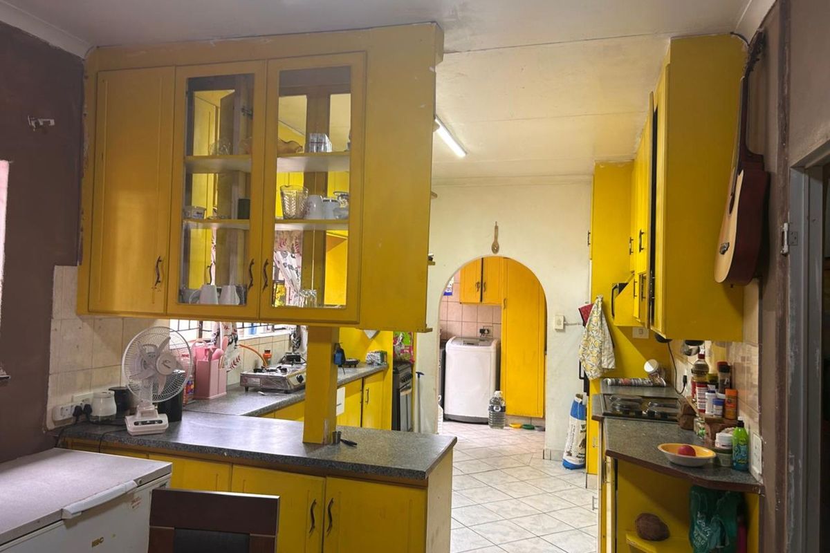 A dated kitchen featuring bright yellow cabinetry, laminate countertops, and a tiled floor, with an arched doorway leading to a secondary utility or laundry area.