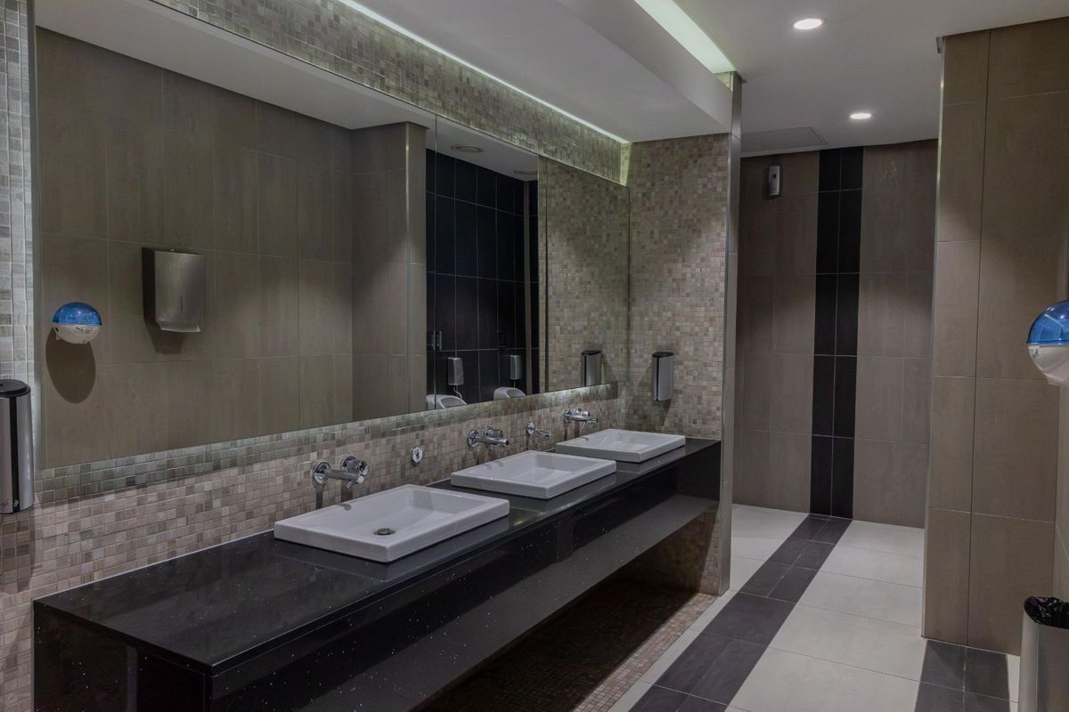 Modern office restroom featuring a triple vanity with vessel sinks, granite countertop, large wall-mounted mirror, and tiled wall finishes.