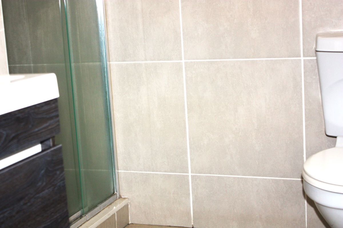 A functional bathroom featuring a glass shower enclosure, a modern vanity unit, and a standard white toilet with neutral wall tiling.
