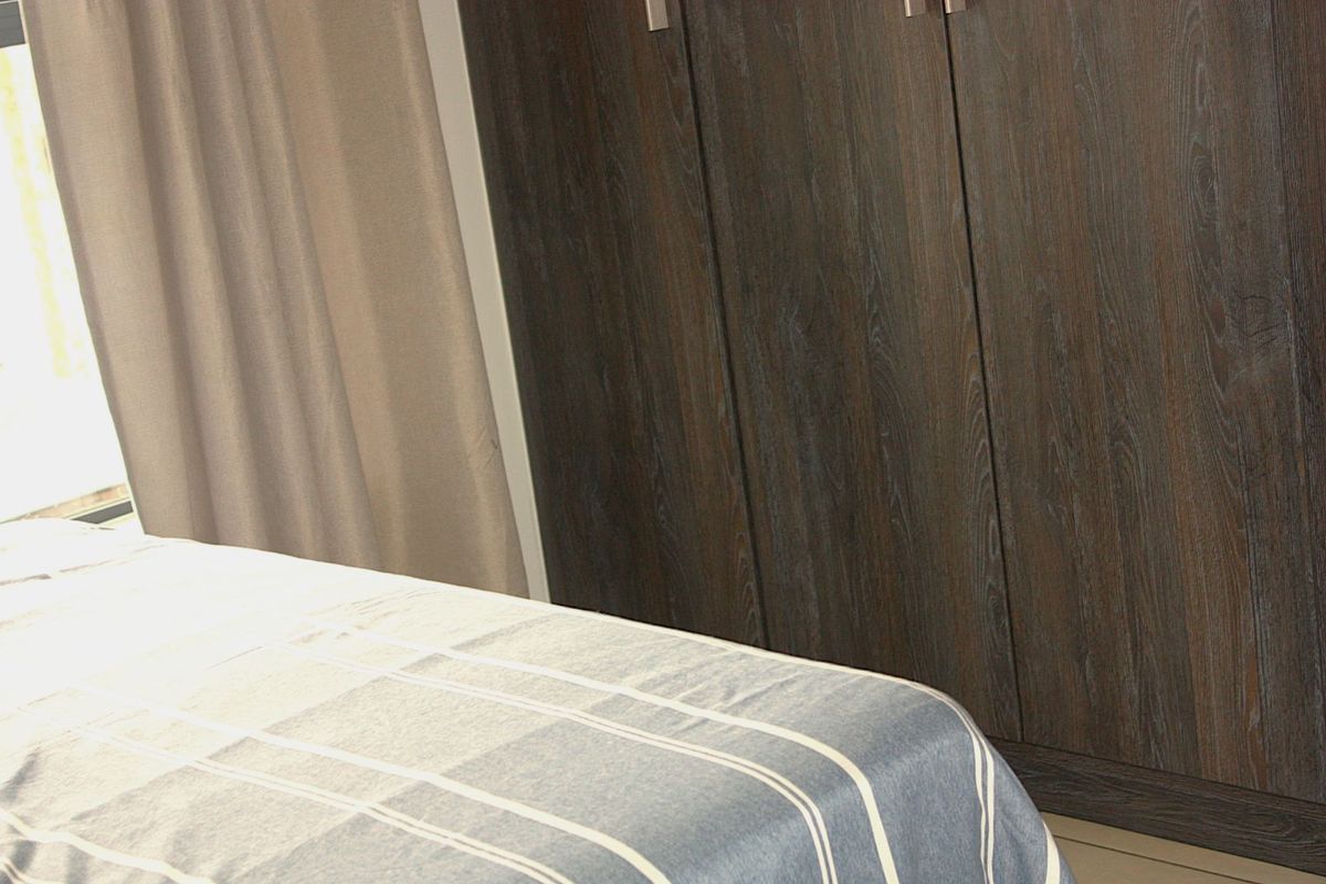 A bedroom featuring dark wood-finish built-in cupboards and natural light from a window.