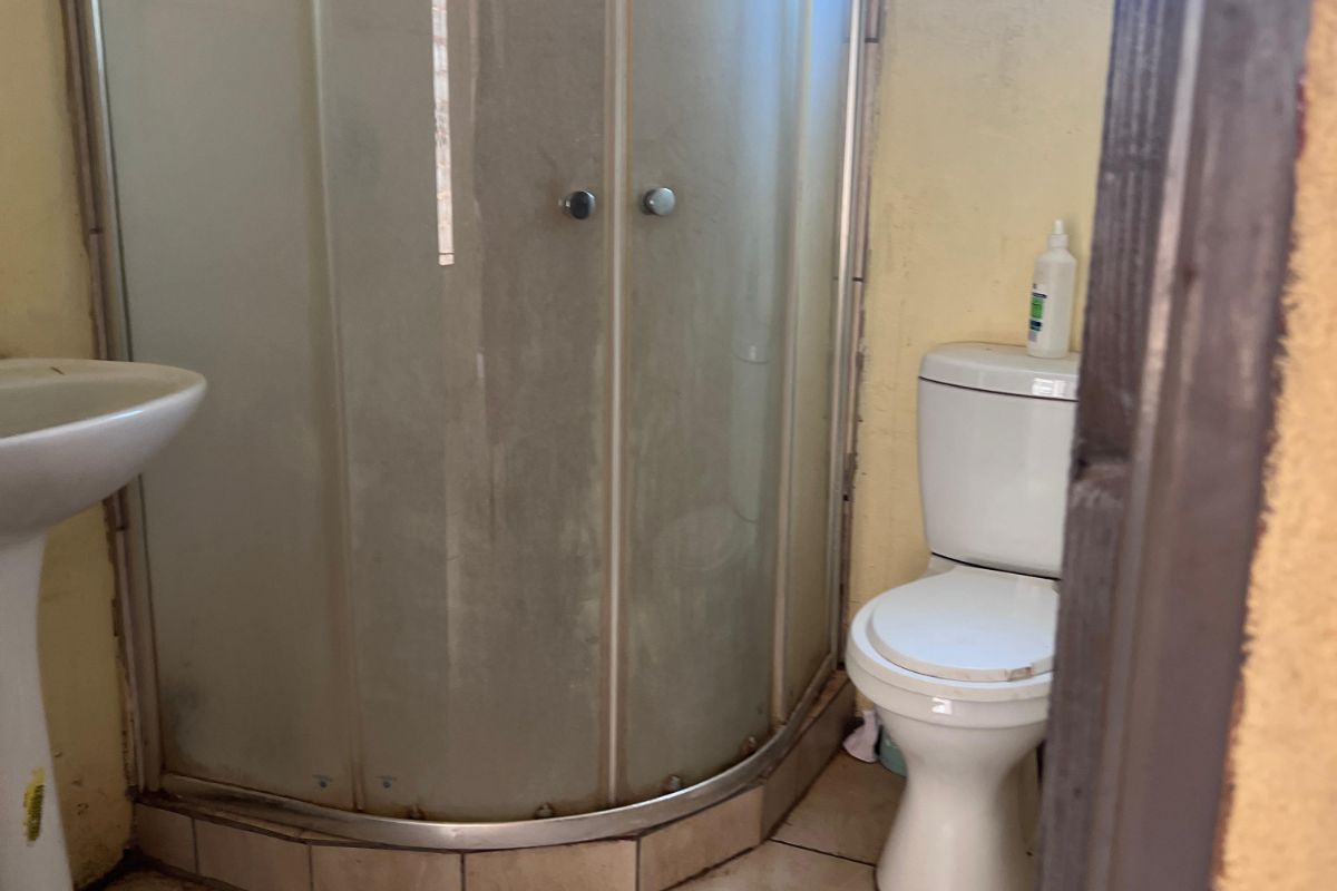 A compact bathroom featuring a corner shower enclosure, pedestal basin, and toilet with tiled flooring and a small window.