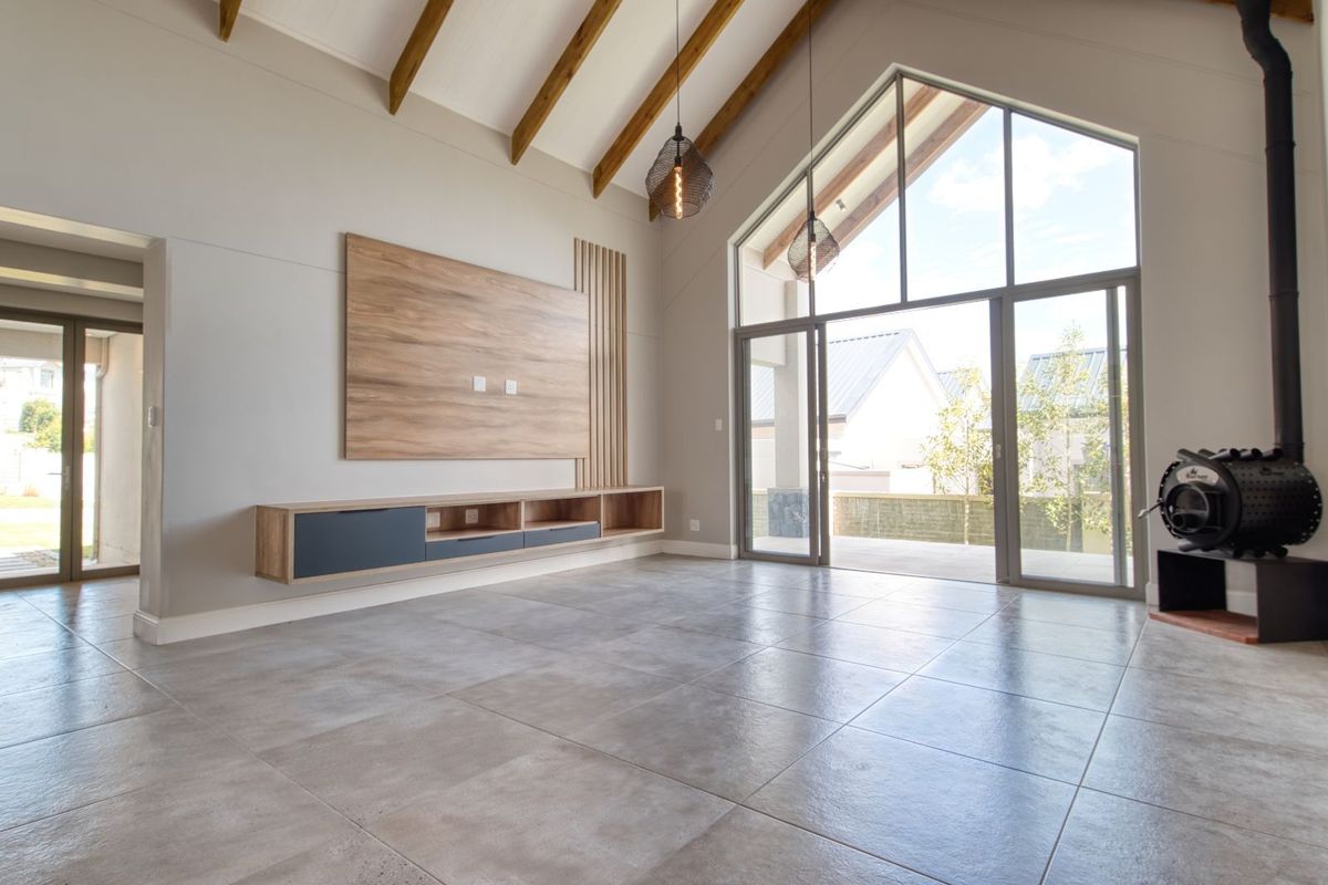 Spacious living area featuring vaulted ceilings with exposed timber beams, large floor-to-ceiling windows, tiled flooring, and a built-in wood-burning fireplace.