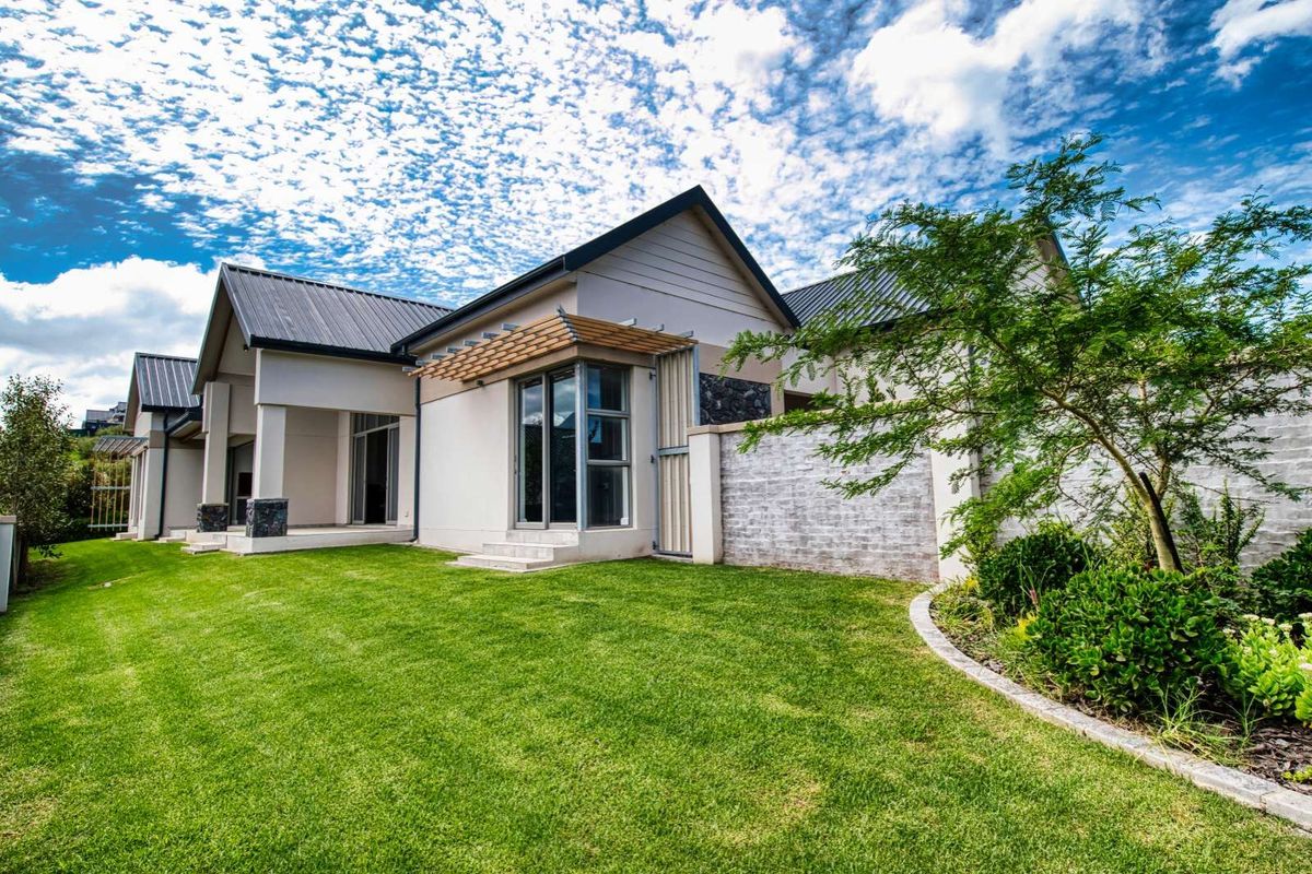 A well-maintained rear exterior view of the house featuring a landscaped lawn, stone-clad feature wall, and covered patio area.