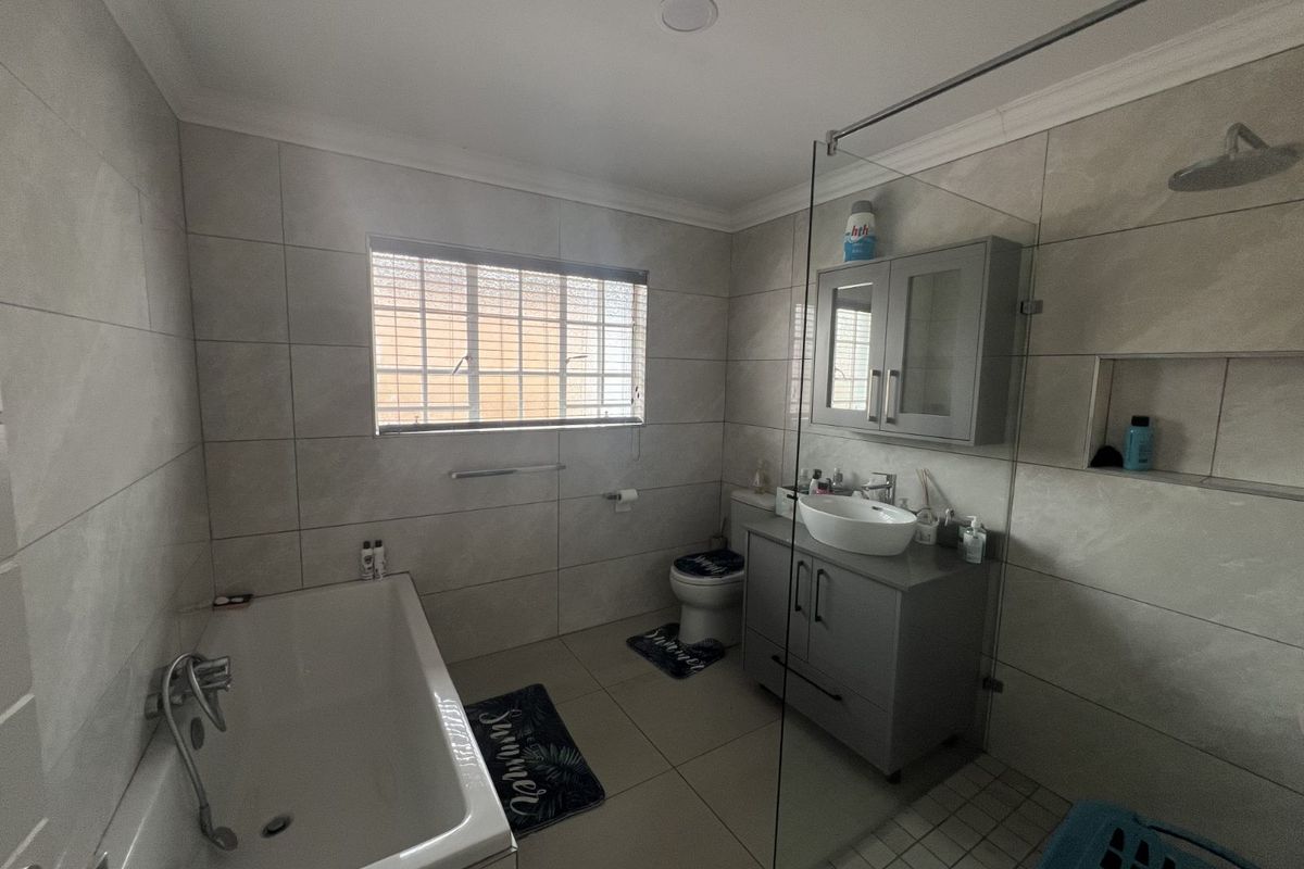 Modern bathroom featuring a glass-enclosed walk-in shower, a separate bathtub, a vanity cabinet with a vessel sink, and neutral wall tiling.