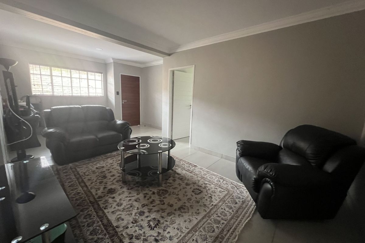 A spacious living room featuring neutral wall tones, tiled flooring, and natural light through a large window.