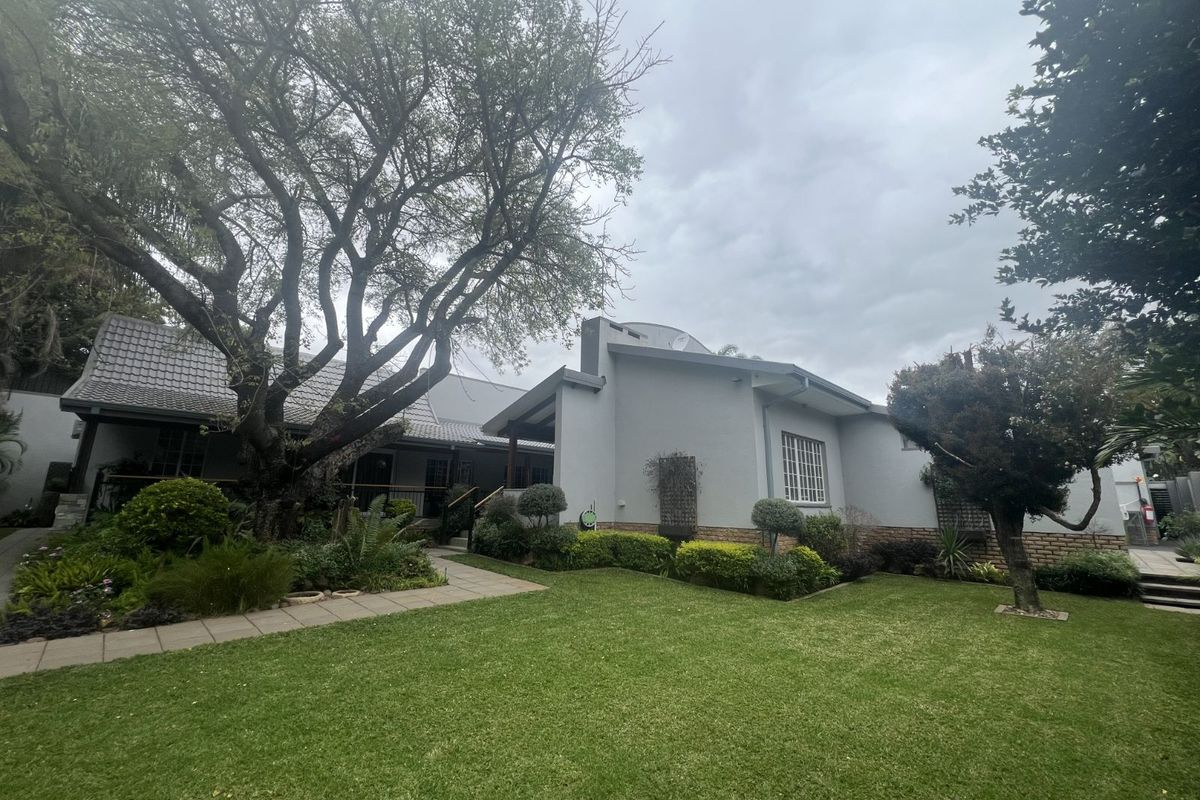 A view of the rear exterior of the house, featuring a well-maintained lawn, landscaped garden, and paved walkway leading to the building.