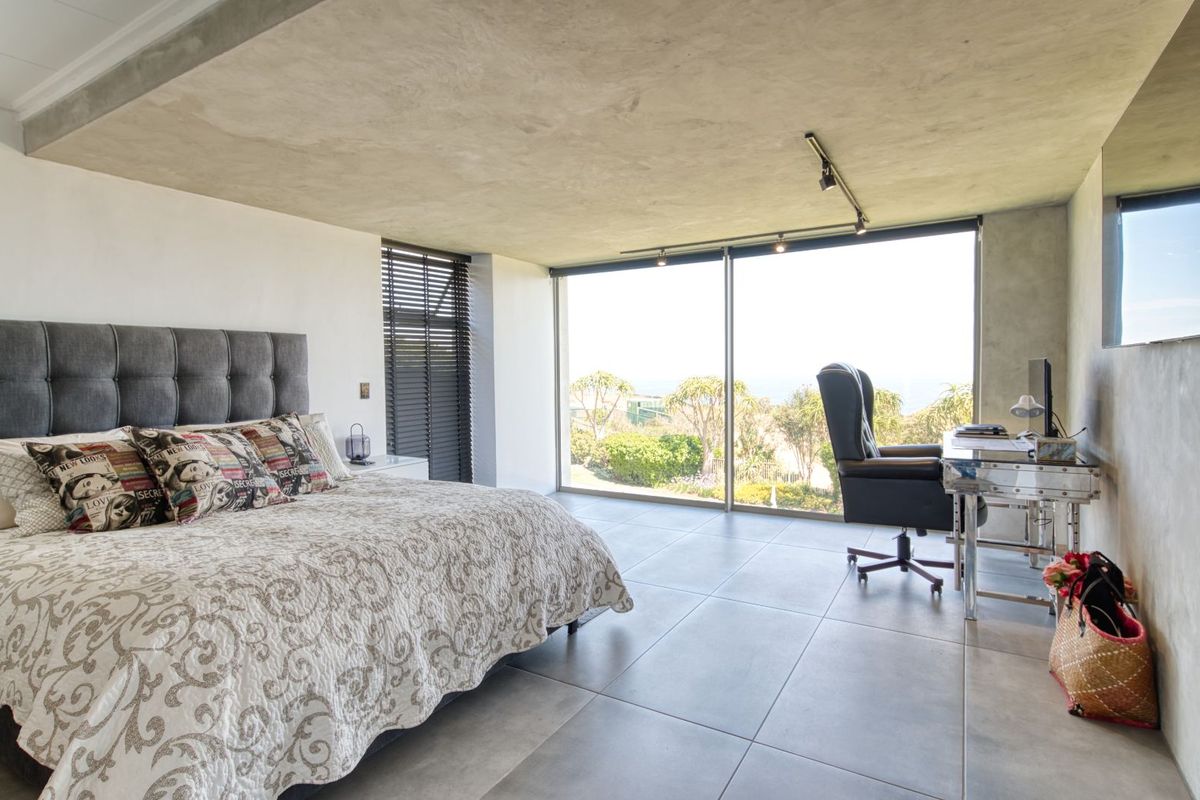 Modern bedroom featuring large floor-to-ceiling sliding glass doors, polished concrete ceiling, and large format floor tiles with expansive views.