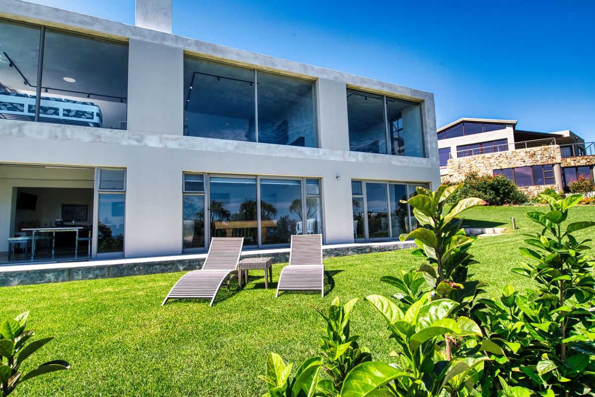 A modern two-story residence featuring expansive glass sliding doors, large windows, and a well-maintained lawn area.