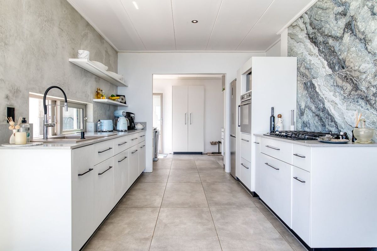 Modern galley-style kitchen featuring white cabinetry, stone-look splashback, integrated oven, gas cooktop, and large format floor tiles.