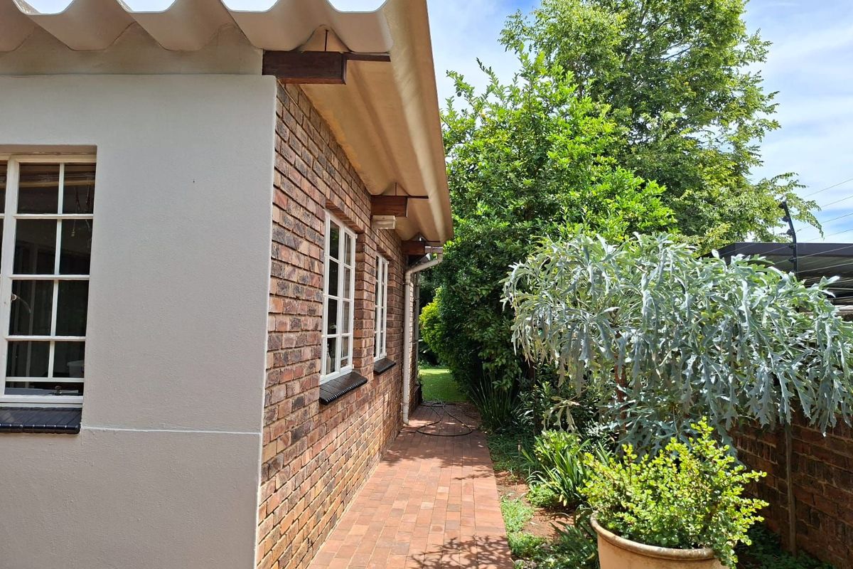 A view of the side exterior of the house featuring exposed brickwork, a paved walkway, and established garden landscaping.